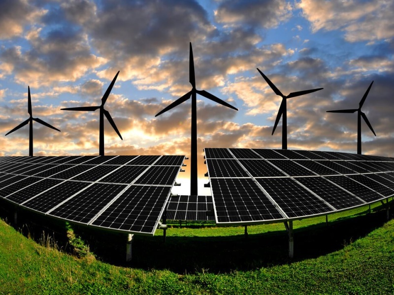 Solar panels and wind turbines at sunset in a field